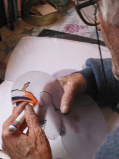 Over shoulder view of an elderly hands holding a market, drawing onto transparent film.
