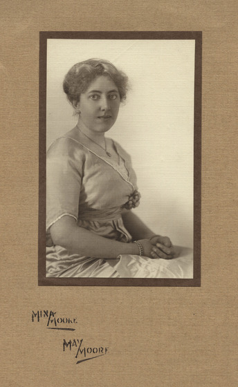 Studio portrait on card, of a woman seated with hands in her lap, wearing a dress, bracelet and pendant necklace.