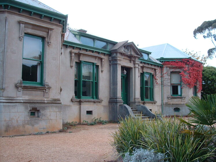 Ornate one story building with vines with bright red leaves growing around one side. Steps feature up to a door, and there are windows all around.