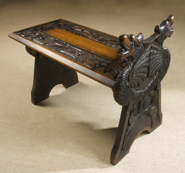 Ornate carved timber boot stool, with two dragon heads carved on the raised side edge.