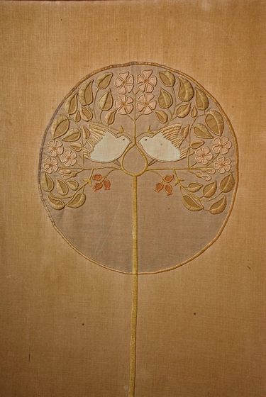 Circulate embroidered design of two blue birds facing, standing on a plant of pink flowers, green leaves, and gum nuts.