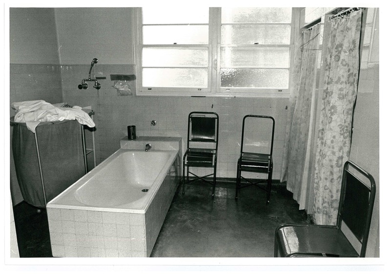 A bathroom within Mont Park. To the left of the bathtub sits a laundry basket. To the right of the bathtub are a number of chairs and two shower units.