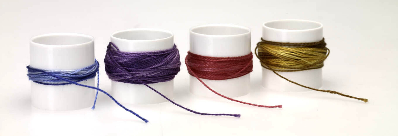 Four acrylic small cylinders, each holding a different coloured thread wrapped around of blue, purple, red and yellow.