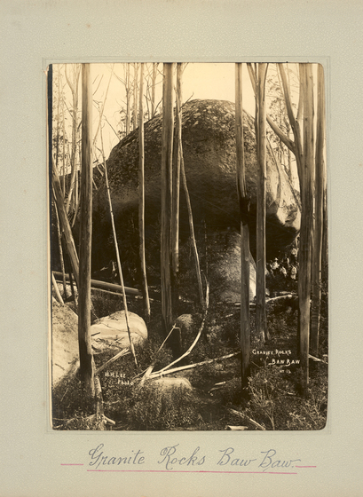 Black and white portrait photograph thin tree trunks in front of a large boulder. Text on the surrounding photo mount reads 'Granite Rocks Baw Baw'