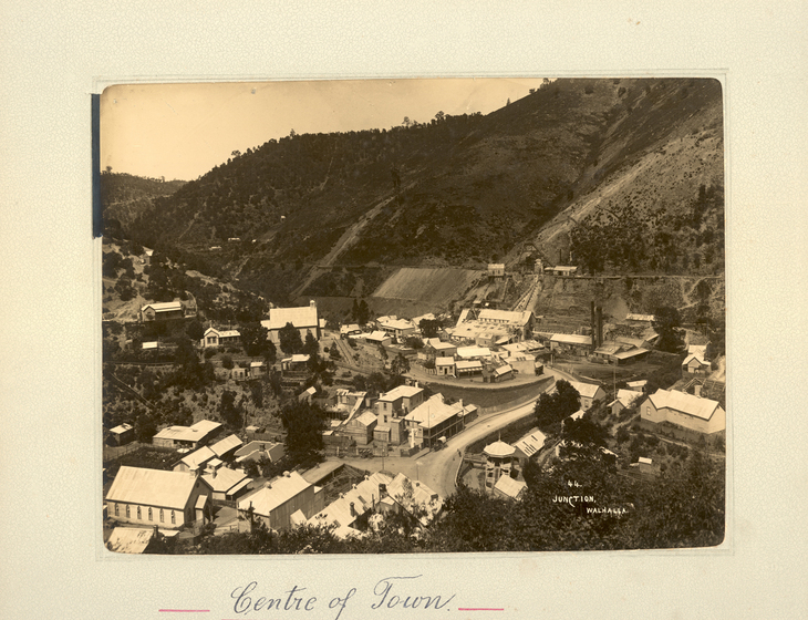 Black and white landscape photograph of a township set at the base of a hillside. Text on the surrounding photo mount reads 'Centre of Town''
