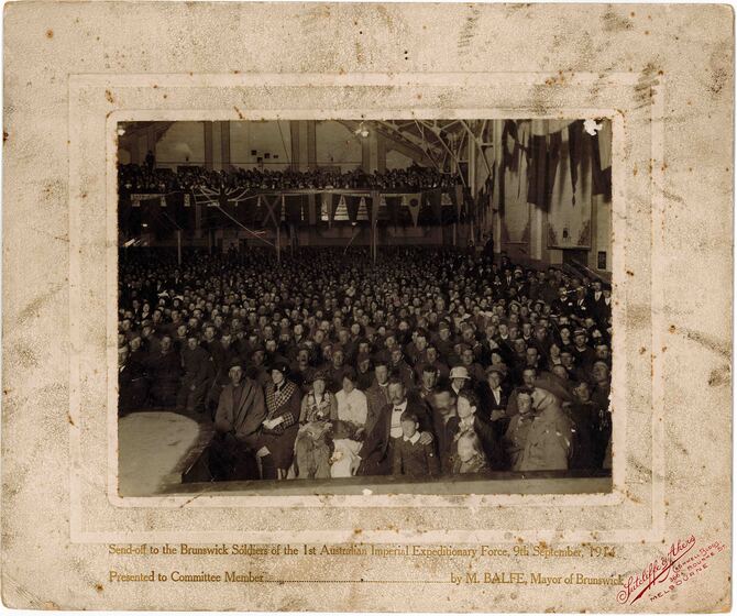 Crowd of people including many soldiers in uniform seated in a hall.