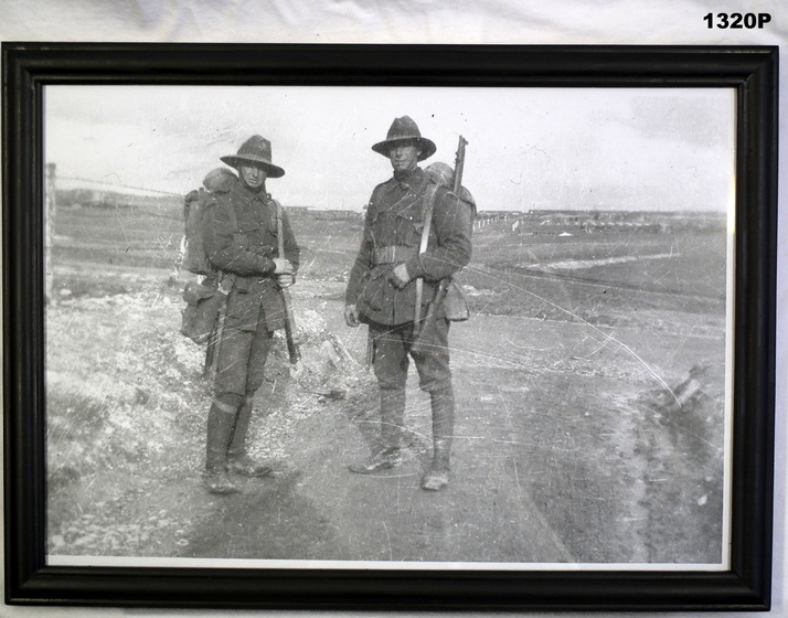 Photograph showing two soldiers in uniform with backpacks and rifles slung over their shoulder on a road.