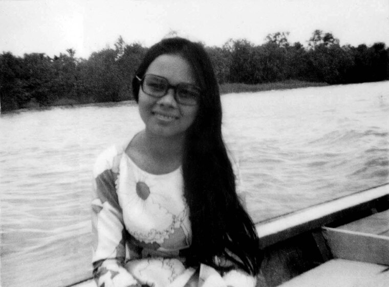 Woman seated in a boat on water, with long hair wearing glasses and a floral print dress.