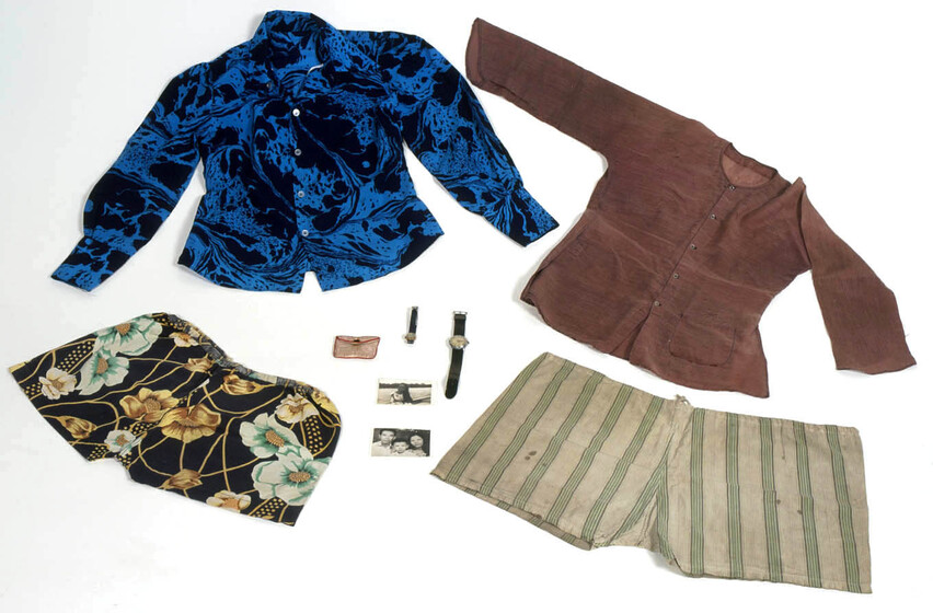 Clothing laid out, featuring a blue and black patterned blouse, brown shirt, floral shorts, striped shorts. Alongside are two black and white photographs, two watches, and a small purse. 