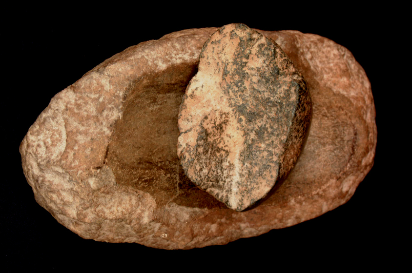 Small stone sitting in a deep impression in a larger stone. Both stones show wear and edging from use.