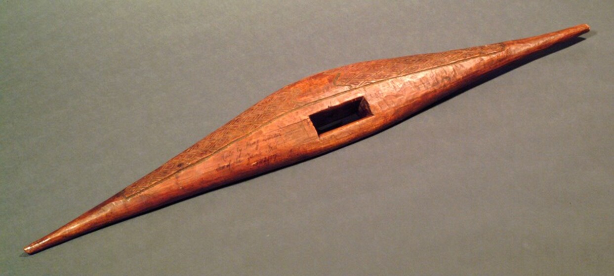 Thin, wooden shield which is narrow at either end, and wider in the centre, with a cut out rectangle hole on one side. 