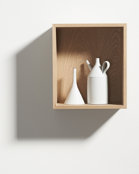 A timber box hung on a white wall to create a shelf. Inside the box is a white flask and white jug with a spout and handle.