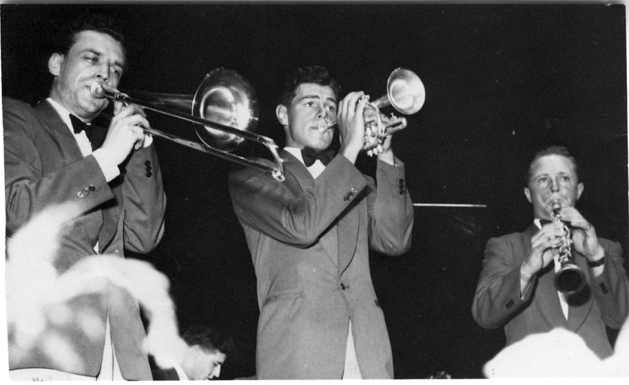 Black and white photo of three men in suits, playing instruments, including from left to right a trombone, trumpet and clarinet.