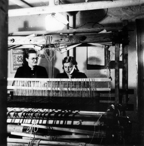 Black and white photograph of two women seated behind a large loom.