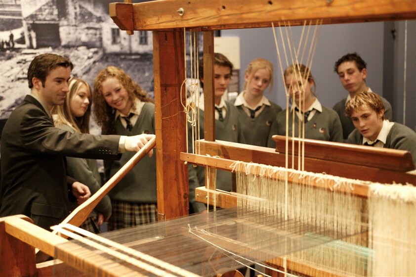 Colour photograph of a group of high school students standing behind a large loom with white thread.