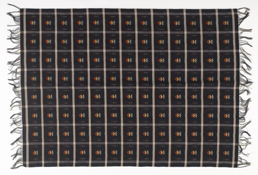 Length of black fabric with fringed edges, making rows of small red motifs.