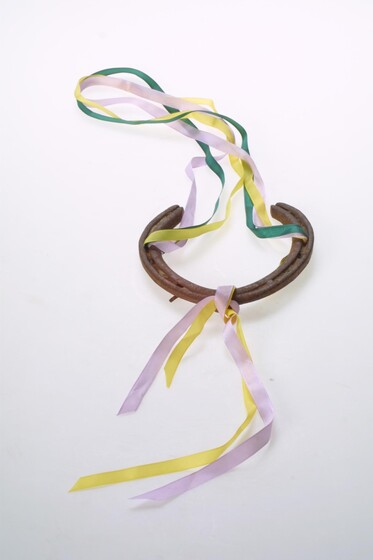 A horseshoe with pink, yellow and green ribbon tied to it.