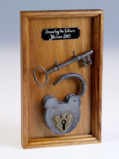 A large metal key and padlock displayed on a wooden board with a plaque above reading 'securing the future Yarram 2003'. 