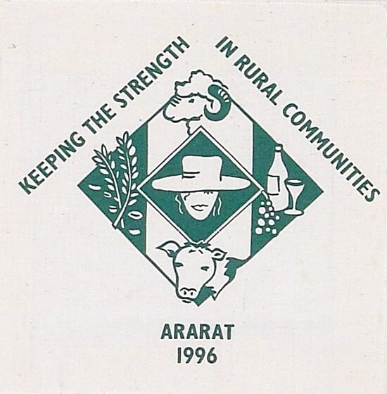 White fabric square printed green diamond shape with a head wearing a hat in the centre, a ram's head above, and a cow's head below. To the left is wheat, and to the right is a bottle, wine glass and grapes. Surrounding the diamonds is the text 'Keeping the strength in rural communities' and 'Ararat 1996'. 