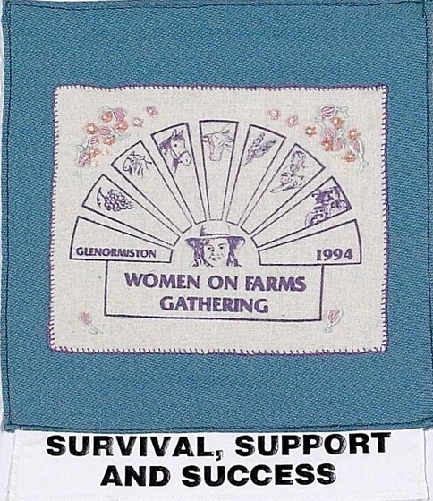 Blue fabric square with a white rectangle down in the middle, featuring a fan shape with different farm motifs on the ends, meeting in the middle with a woman's face centre. beneath is text 'women on farms gathering'. Sewn to the bottom of the patch is a white strip of fabric with black text 'survival, support and success'.