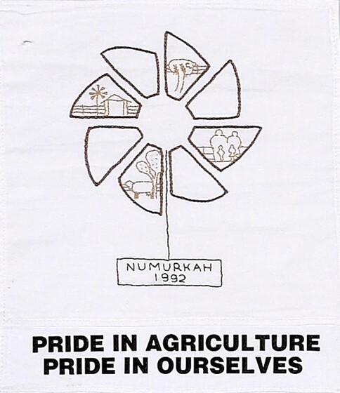 White fabric square with a stylized windmill inside which are images of farm scenes. Below is text 'Numurkah 1992 and Pride in Agriculture Pride in Ourselves'. 