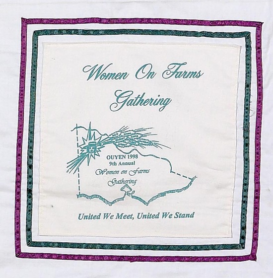 White fabric square with purple and green border. In the middle is a line shape of the state of Victoria with wheat overlaying it. Text above reads 'Women on Farms Gathering'. Text below reads 'United we meet, united we stand'. 