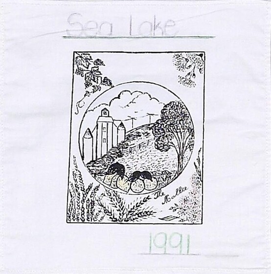 White fabric square with a black line drawing of a farm in a circle, within a rectangle featuring grape vines, gumnut blossoms and wheat. Above is text 'Sea Lake', below is text '1991.  