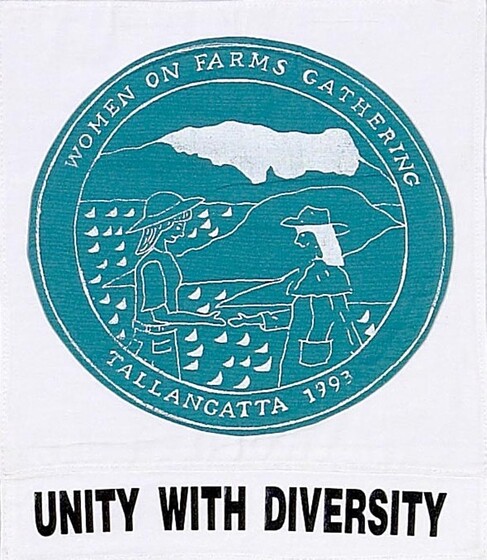 White fabric square with a green circle with white line drawing of two women standing in front of rocky water edge. Surrounding the image is text, 'Women on farms gathering, Tallangatta 1993'. Below is text Unity with Diversity'. 