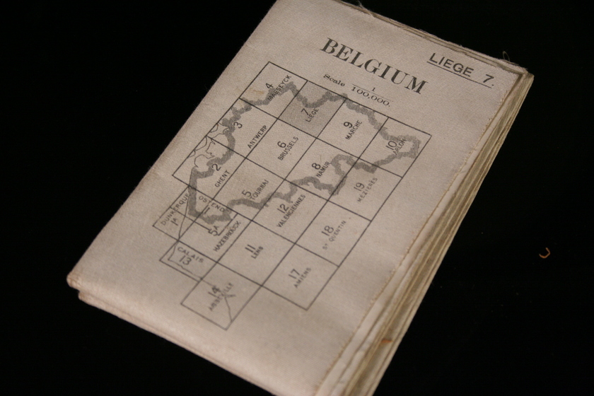 Folded white paper map on a black background, with text 'Belgium and a handrawn map area over a grid pattern on the section of the map that is visible.