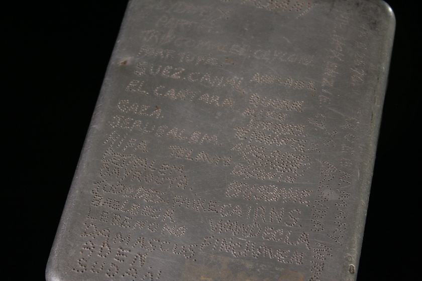 Close up view of a metal rectangular box viewed from above. There is writing engraved across the entire top of the box.