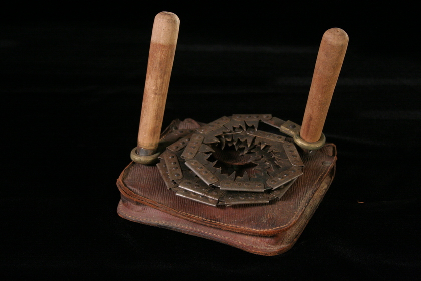 Coiled hand-held saw, with two wooden handles, and the teeth of the metal saw coiled around to form circles. The saw is sitting on a leather pouch.