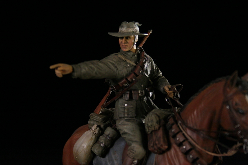 Close up view of a figurine of a man seated on a brown horse in a military army uniform, pointing to the left.