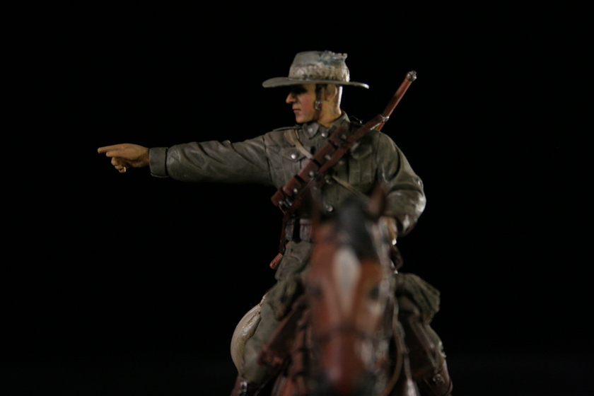 Close up view of a figurine of a man seated on a brown horse in a military army uniform, viewed from front on to the horse's head. The man is pointing to the left.