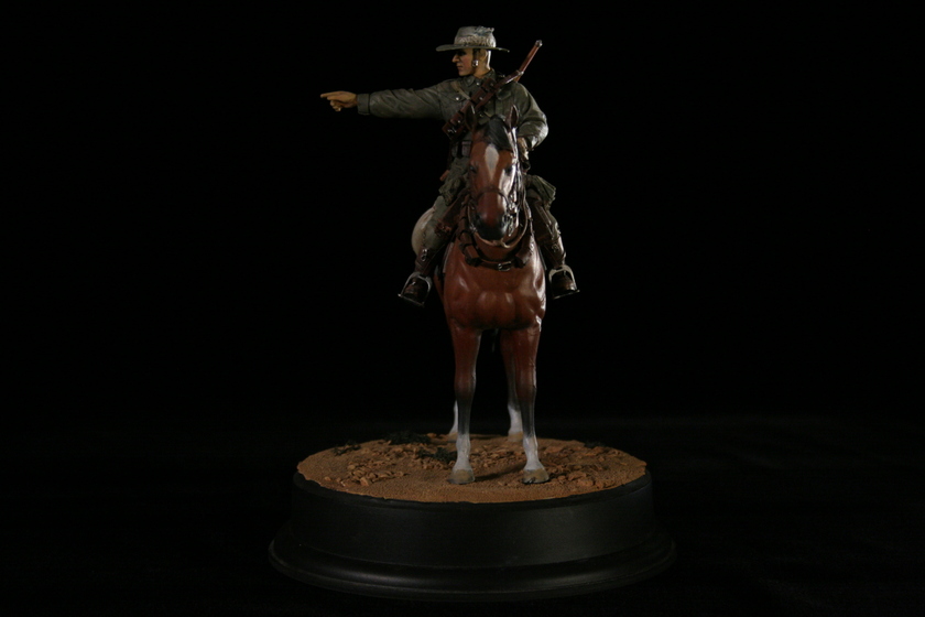 A figurine of a man seated on a brown horse in a military army uniform, viewed from front on to the horse's head. The man is pointing to the left.