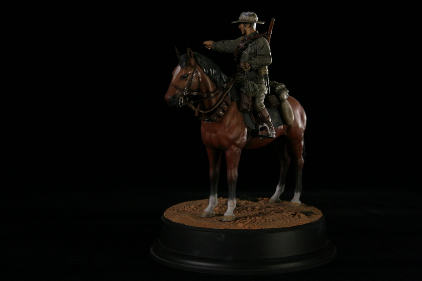 Close up view of a figurine of a man seated on a brown horse in a military army uniform, viewed from the left side of the horse. The man is pointing to the left.