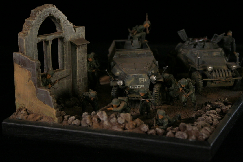 A model of two armored military vehicles sitting in a building, behind a group of men wearing military army uniforms crouched behind a crumbled wall. 