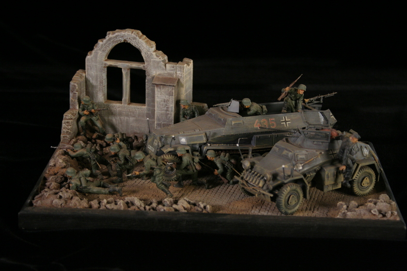 A model of two armored military vehicles sitting in a building, behind a group of men wearing military army uniforms crouched behind a crumbled wall. 