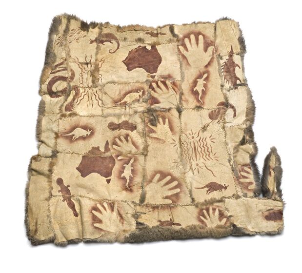 Underside of possum skins stiched together to make one panel. Across the skin are painted images of hands, the landmass known as Australia, kangaroos, snakes, possums and platypuses.