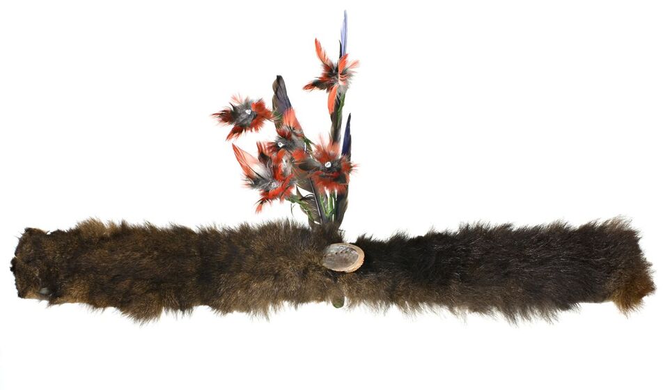 Band of possum skin with a small shell in the centre. Placed behind the shell is a small collection of red and green feathers fashioned to look like flowers and leaves.