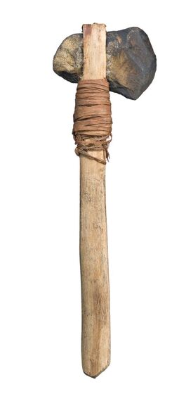 Stone hand axe with a wooden handle. The stone head is wedged into the stone handle at the top, beneath leather string is wrapped around the handle.