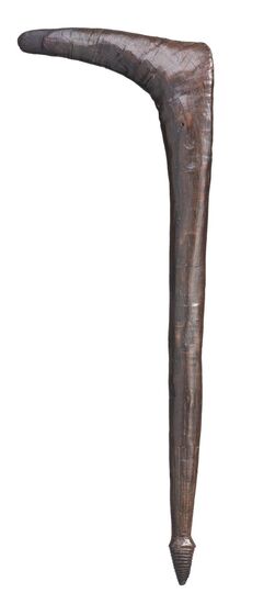 Wooden club with a thin handle made from dark brown timber, which bends at right angles at the top to the left. 