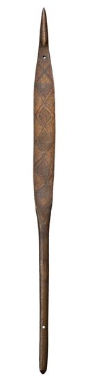 Spearthrower made from light wood, carved in a long thin shape which is wider in the middle. At the top is a small circular hole in the wood. Across the surface is a pattern of diamonds.