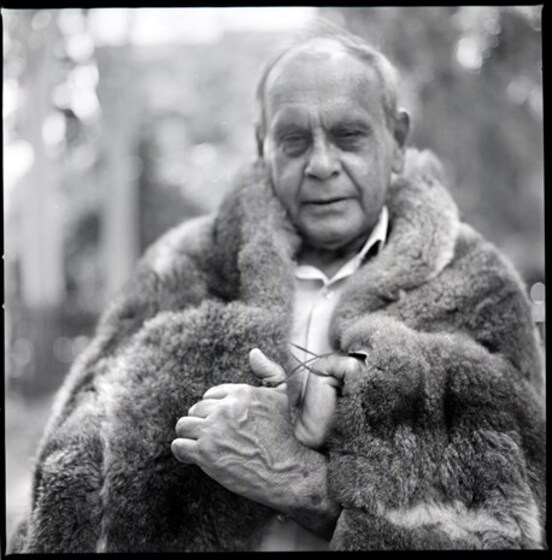 Close up photograph of an older man with a possum skin cloak wrapped around his shoulders.
