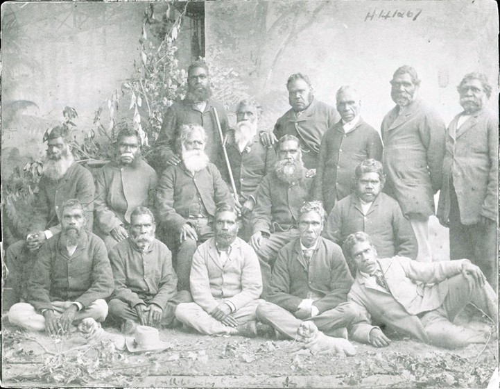 Black and white studio photograph of a group of men wearing suits seated and standing in three rows.