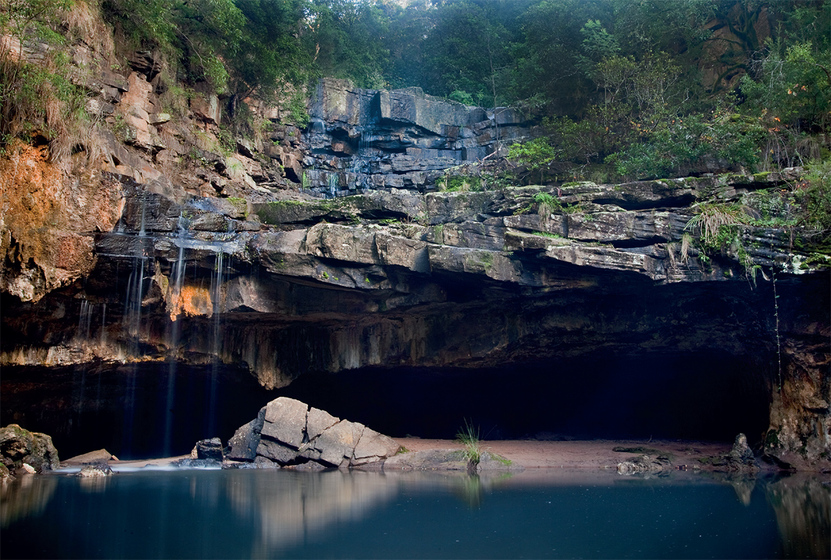 water spills over a rock ledge leading to a cave