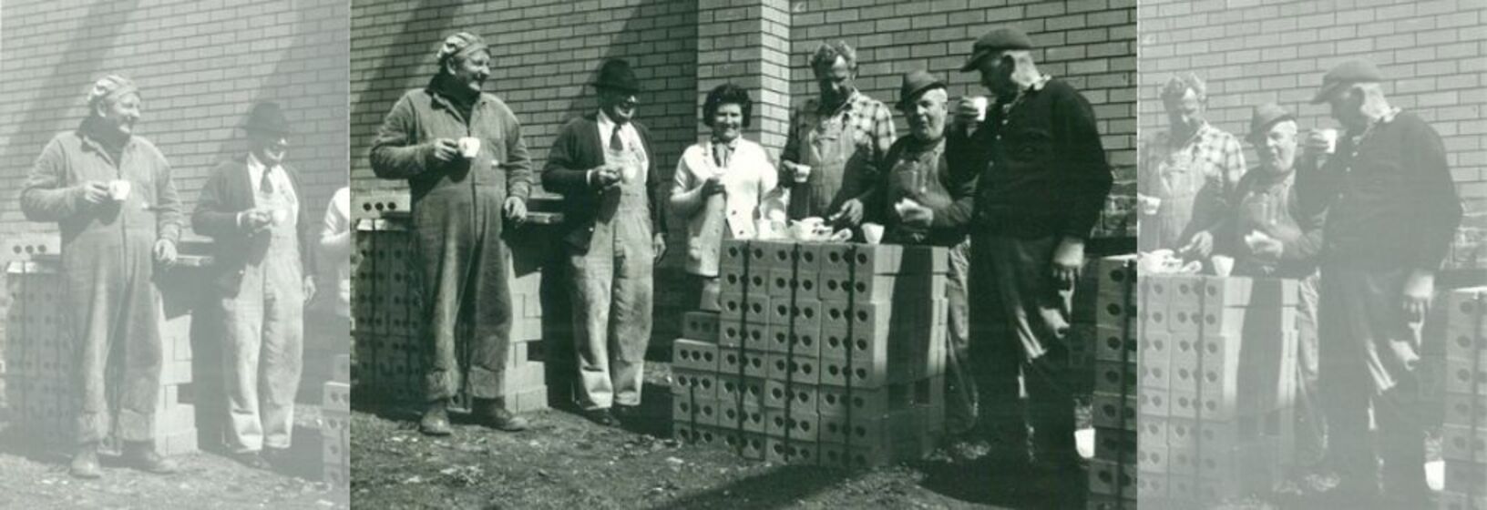 Five men and one woman share a meal on a pile of new bricks at a construction site