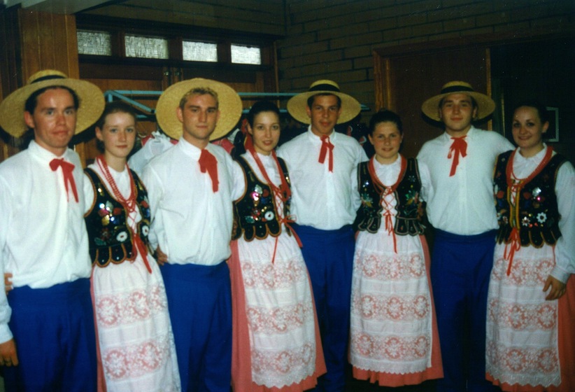 Four couples stand arm in arm in matching traditional colouful Polish costumes