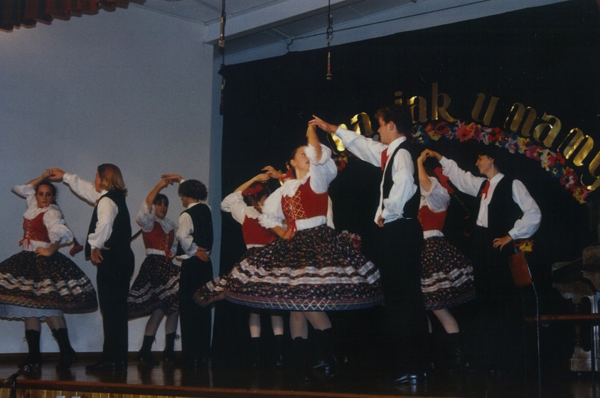 A group of ten dancers in colourful traditional Polish costumes perform on stage