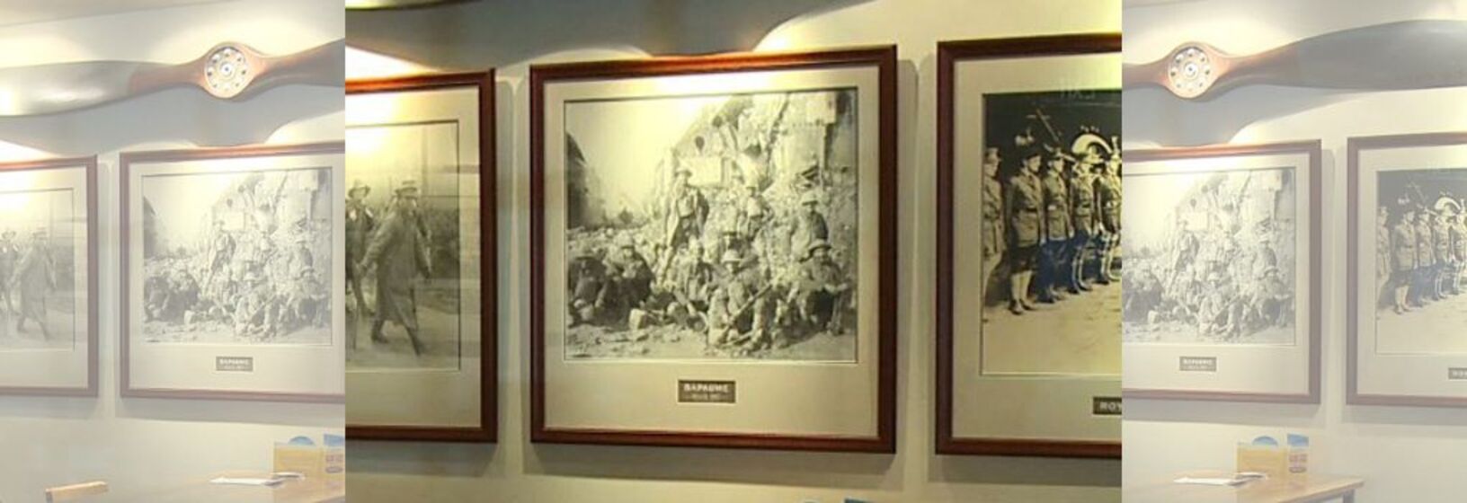 Series of framed black and white photographs on a wall with a propeller mounted above.