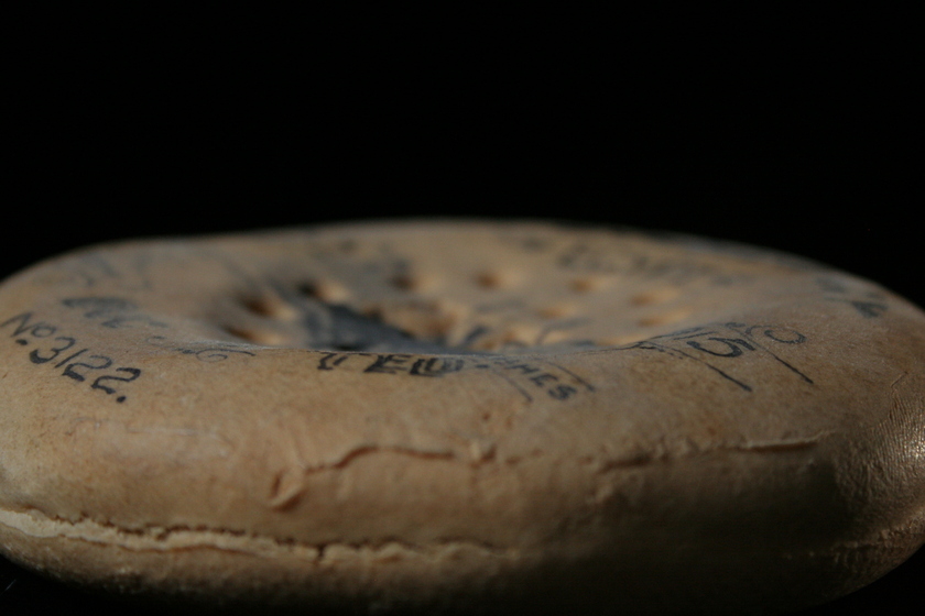 Side view of a round biscuit laying down on a black background, covered in ink writing and illustrations.